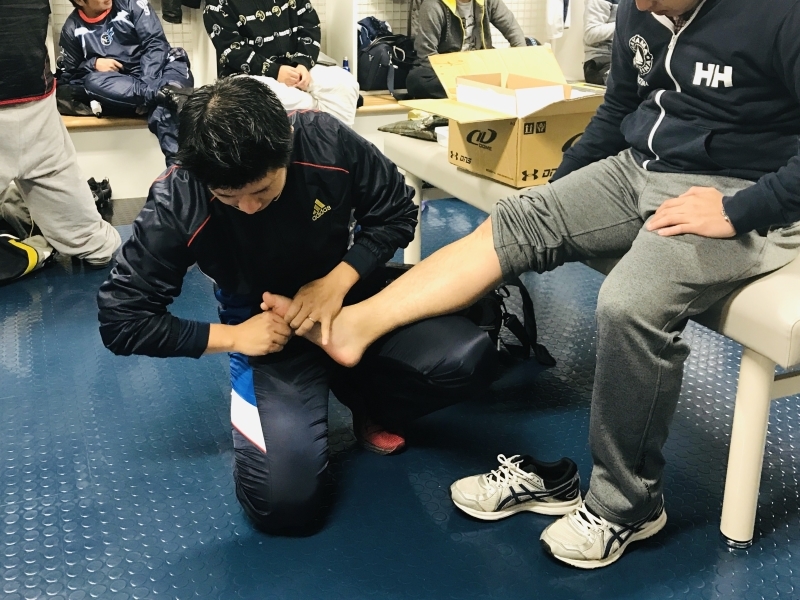 スポーツ現場で足部の状態を確認しながら調整を行っている様子（アストケア）